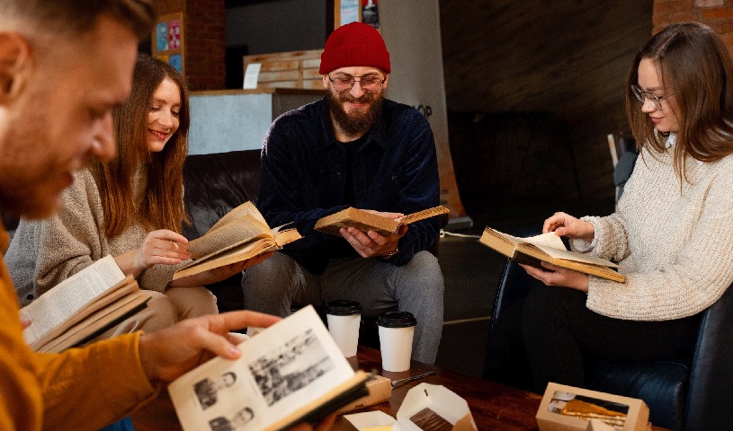 A diverse group of people sitting together, sharing old photographs and journals in a welcoming, collaborative workshop setting